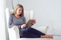 Woman sitting on white armchair with tablet computer