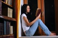 Woman is sitting on window and reading