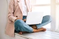 Woman sitting at windowsill and working at laptop.