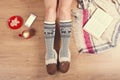 Woman sitting on the wooden floor with cup of coffee, phone, cookie and book. Close-up of female legs in warm socks with a deer vi Royalty Free Stock Photo