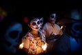 Woman with skull and spiderweb make-up and dress with traditional mexican flowers surrounded by costumed people at the parade for