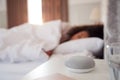 Woman Sleeping In Bed With Voice Assistant On Bedside Table Next To Her