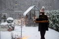 Woman in sleepwear and hat goes out on her snowy backyard