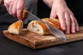 Woman Slices Homemade Wholemeal Multigrain Bread with Flax Seeds and Sesame on Wooden Board on Dark Table