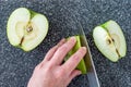 Woman slicing a green Granny Smith apple on a plastic man made faux gray granite cutting board, hands and chefs knife, apple halve Royalty Free Stock Photo