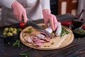 Woman slicing Spanish fuet salami sausageon wooden cutting board at domestic kitchen