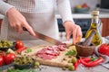 Woman slicing Spanish sausage fuet salami with knife on a domestic kitchen