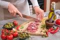 Woman slicing Spanish sausage fuet salami with knife on a domestic kitchen