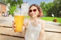 Woman with slim figure drinks freshly squeezed orange juice from a plastic cup. Useful and harmful beverages