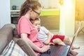 Woman with a small child on knees is sitting at a laptop. Remote work and receiving online education of home