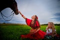 A woman and a girl in bright Gypsy dresses with a horse in a field with green grass. Mother and daughter pose in nature with an