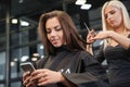 Woman with smartphone and hairdresser making hair styling at salon Royalty Free Stock Photo