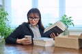 Woman with smartphone unpacking box with books, online shopping Royalty Free Stock Photo