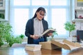 Woman with smartphone unpacking box with books, online shopping Royalty Free Stock Photo