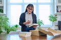 Woman with smartphone unpacking box with books, online shopping Royalty Free Stock Photo