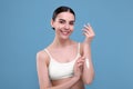 Beautiful woman with smear of body cream on her arm against light blue background Royalty Free Stock Photo