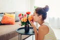 Woman smelling fresh roses in vase on table. Housewife taking care of coziness in apartment. Interior and decor