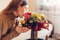 Woman smells fall bouquet made of red yellow orange flowers arranged in vase at home. Fresh blooms in autumn colors Royalty Free Stock Photo