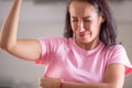 Woman smells herself with repulsive facial expression and sweat patches on her pink shirt