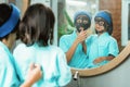 a woman smiles while cleaning a black clay face mask with a little girl in front of the mirror Royalty Free Stock Photo