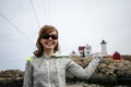 Woman smiles and holds the Nubble Lighthouse in a forced perspective view