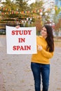 A woman smiles and holds a poster with the text Study in Spain