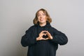 A woman smiling at the camera and shapping a heart with her hands is showing her love