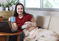 Woman smiling and looking at camera , holding blue cup of coffee,  sitting on couch in living room with computer in front of her Royalty Free Stock Photo