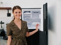 Woman smiling with teeth looking into camera in kitchen at home opened freezer empty with ice inside, home refrigerator