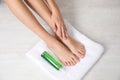 Woman with smooth feet, white towel and cosmetic on light background, top view