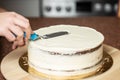 Woman smoothing edges of a chocolate cake covered with whipped cream, with a spatula, in the kitchen