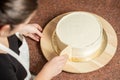 Woman smoothing edges of a chocolate cake covered with whipped cream, using a cake smoother tool