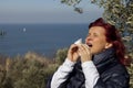 Woman sneezing, blowing nose into tissue above sea coast