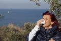 Woman sneezing, blowing nose into tissue above sea coast