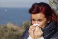 Woman sneezing, blowing nose into tissue above sea coast