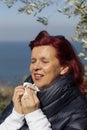 Woman sneezing, blowing nose into tissue above sea coast