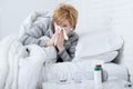 Woman with sneezing nose blowing in tissue on bed suffering cold flu virus symptoms having medicines tablets pills