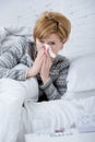 woman with sneezing nose blowing in tissue on bed suffering cold flu virus symptoms having medicines tablets pills Royalty Free Stock Photo