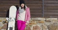 Woman with snowboard near building wall