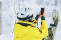 Woman snowboarder in bright suit in a sports helmet photographed on a smartphone. Travel blogger. Extreme sports. Active rest.