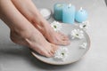 Woman soaking her feet in bowl with water and flowers on grey marble floor, closeup. Pedicure procedure Royalty Free Stock Photo