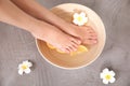 Woman soaking her feet in bowl with water, orange slices and flower on grey background, top view Royalty Free Stock Photo