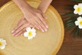 Woman soaking her hands in bowl with water and flowers on wooden table. Spa treatment Royalty Free Stock Photo