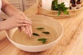 Woman soaking her hands in bowl of water and leaves on wooden table, closeup. Spa treatment Royalty Free Stock Photo