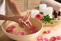 Woman soaking her hands in bowl of water and petals on table, closeup. Spa treatment Royalty Free Stock Photo