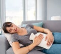 Woman, sofa and pain with hot water bottle in home, abdominal cramps or menstrual issues. Endometriosis, cyst ovaries or