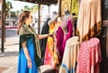 Woman in souk. Tourist looking at traditional Arabian dresses and clothes in store or outdoor market.