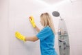 Woman with special cleaning sponge cleaning wall tiled surface in bathroom. Royalty Free Stock Photo