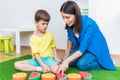 A woman speech therapist deals with a boy and performs an exercise to correct the speech apparatus by playing on the floor