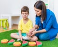 A woman speech therapist deals with a boy and performs an exercise to correct the speech apparatus by playing on the floor